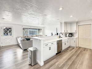 Kitchen with kitchen peninsula, sink, dishwasher, white cabinets, and light hardwood / wood-style floors