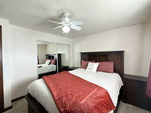 Carpeted bedroom featuring ceiling fan, a closet, and a textured ceiling