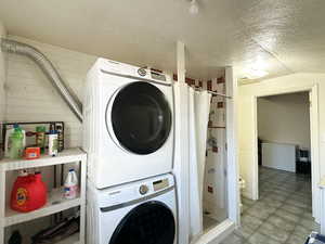 Laundry area featuring a textured ceiling and stacked washer and clothes dryer