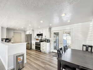 Kitchen with french doors, light hardwood / wood-style flooring, a textured ceiling, appliances with stainless steel finishes, and white cabinetry