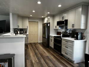 Kitchen featuring a textured ceiling, kitchen peninsula, dark wood-type flooring, and appliances with stainless steel finishes