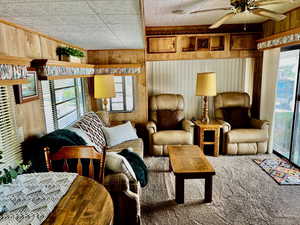 Carpeted living room featuring ceiling fan and wooden walls