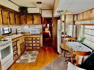 Kitchen with wood walls, light wood-type flooring, white appliances, and sink