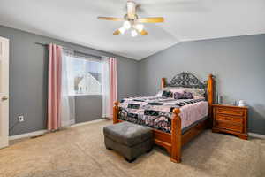 Carpeted bedroom featuring ceiling fan and vaulted ceiling