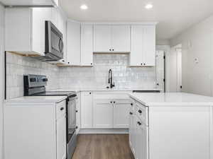 Kitchen with tasteful backsplash, stainless steel appliances, dark wood-type flooring, sink, and white cabinetry