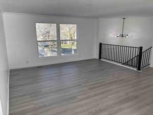 Empty room with wood-type flooring, an inviting chandelier, and crown molding