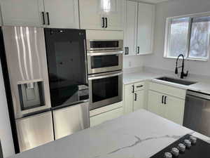 Kitchen with white cabinetry, light stone counters, sink, and stainless steel appliances