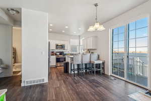 Kitchen featuring stainless steel appliances, white cabinetry, a breakfast bar, dark wood-type flooring, and pendant lighting