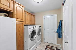 Laundry room with light tile patterned flooring, cabinets, a textured ceiling, and washing machine and clothes dryer