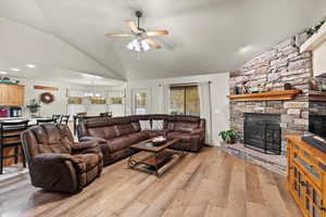 Living room with a fireplace, light wood-type flooring, ceiling fan with notable chandelier, and lofted ceiling