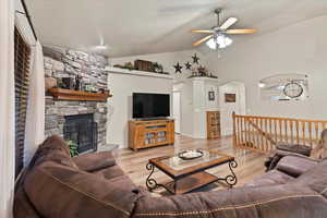 Living room with high vaulted ceiling, light hardwood / wood-style flooring, ceiling fan, and a stone fireplace