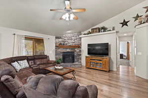 Living room featuring a fireplace, light wood-type flooring, high vaulted ceiling, and ceiling fan