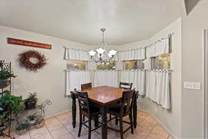 Tiled dining space featuring a textured ceiling and a notable chandelier