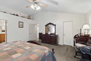 Bedroom featuring ceiling fan, dark carpet, lofted ceiling, and connected bathroom