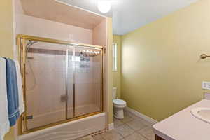 Full bathroom featuring tile patterned floors, vanity, enclosed tub / shower combo, and toilet