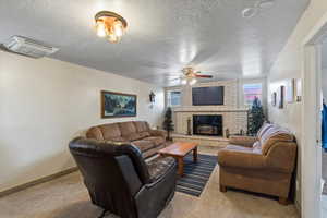 Living room with ceiling fan, a wood stove, a textured ceiling, and light carpet