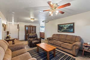 Living room with ceiling fan, a textured ceiling, and light carpet