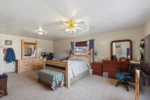 Bedroom with stainless steel refrigerator, ceiling fan, light carpet, and a textured ceiling