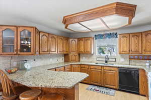 Kitchen with dishwasher, a kitchen breakfast bar, sink, light stone counters, and kitchen peninsula