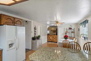 Kitchen featuring ceiling fan, light wood-type flooring, a textured ceiling, white fridge with ice dispenser, and light stone counters