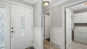 Tiled entrance foyer with crown molding and washer / dryer