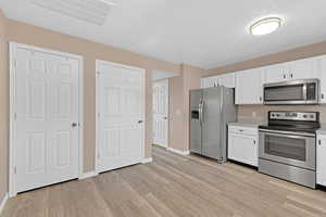 Kitchen featuring white cabinetry, light hardwood / wood-style flooring, a textured ceiling, and appliances with stainless steel finishes