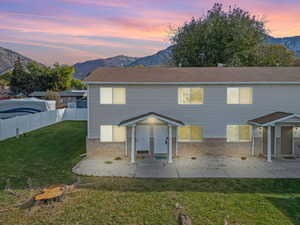 Front of house at dusk with a lawn, a patio area, and a mountain view