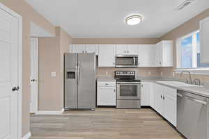 Kitchen featuring stainless steel appliances, white cabinetry, light hardwood / wood-style floors, and sink