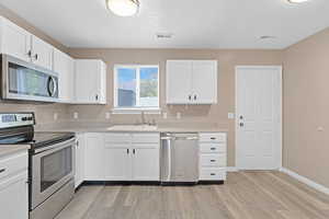 Kitchen featuring white cabinets, light wood-type flooring, sink, and appliances with stainless steel finishes