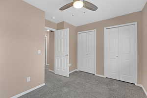 Unfurnished bedroom featuring ceiling fan, light colored carpet, and two closets