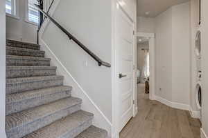 Staircase with hardwood / wood-style flooring and stacked washer / drying machine