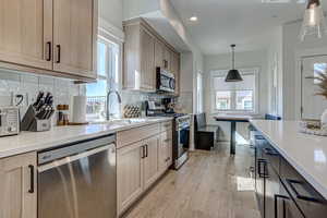 Kitchen with light brown cabinets, light hardwood / wood-style floors, hanging light fixtures, and appliances with stainless steel finishes