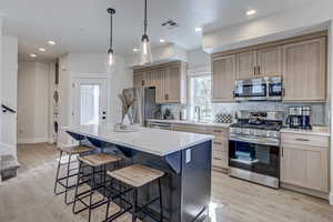 Kitchen featuring sink, light wood-type flooring, appliances with stainless steel finishes, a kitchen island, and stacked washer / dryer