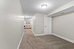 Corridor featuring light colored carpet and a textured ceiling