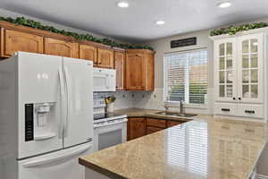 Kitchen with sink, decorative backsplash, white appliances, a textured ceiling, and kitchen peninsula