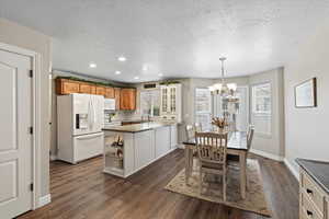 Kitchen featuring kitchen peninsula, white appliances, dark wood-type flooring, sink, and hanging light fixtures