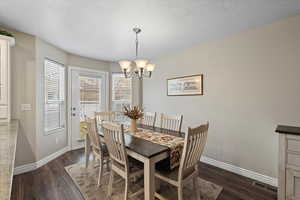 Dining space with a textured ceiling, a chandelier, and dark hardwood / wood-style floors