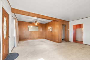 Empty room with light carpet, ceiling fan, and wood walls