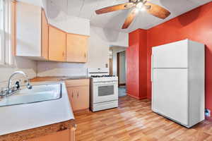 Kitchen featuring light wood-type flooring, white appliances, ceiling fan, and sink