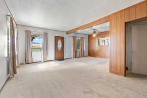 Unfurnished living room featuring ceiling fan, light colored carpet, and wooden walls