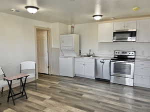 Kitchen featuring sink, stacked washer / drying machine, dark hardwood / wood-style flooring, white cabinetry, and stainless steel appliances