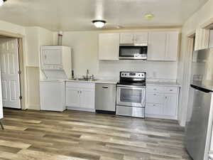 Kitchen featuring appliances with stainless steel finishes, stacked washing maching and dryer, dark wood-type flooring, sink, and white cabinets