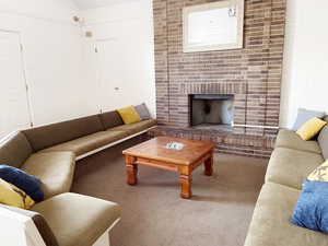 Living room with carpet, vaulted ceiling, and a brick fireplace