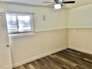 Unfurnished room with ceiling fan, wood walls, and dark hardwood / wood-style flooring