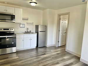 Kitchen featuring sink, white cabinetry, stainless steel appliances, and dark wood-type flooring