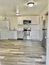 Kitchen with stacked washer / dryer, white cabinetry, and appliances with stainless steel finishes