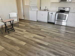 Kitchen featuring sink, stacked washer and dryer, dark hardwood / wood-style floors, white cabinetry, and stainless steel appliances