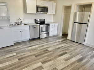 Kitchen with white cabinetry, light hardwood / wood-style floors, stacked washer / drying machine, and appliances with stainless steel finishes