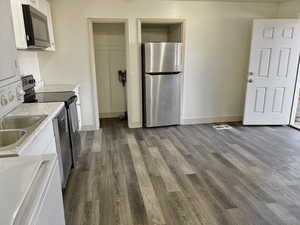 Kitchen with sink, stainless steel appliances, dark hardwood / wood-style flooring, stacked washer and dryer, and white cabinets