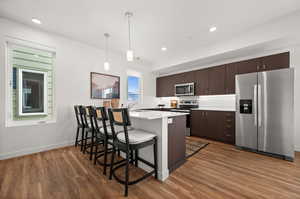 Kitchen featuring hardwood / wood-style flooring, dark brown cabinets, decorative light fixtures, and appliances with stainless steel finishes